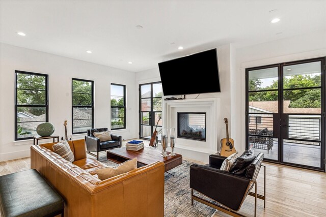 living area with baseboards, recessed lighting, light wood-style floors, and a glass covered fireplace