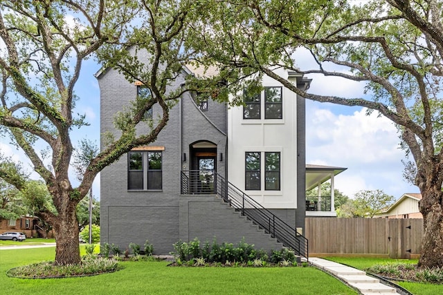 view of front of house with a front lawn, stairs, brick siding, and fence