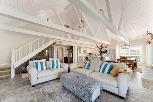 living area featuring a notable chandelier, stairway, light wood-style flooring, and beamed ceiling