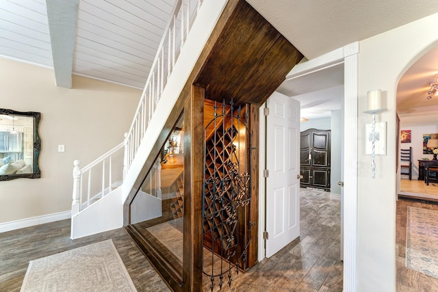 wine area featuring baseboards, arched walkways, wood finished floors, and vaulted ceiling with beams