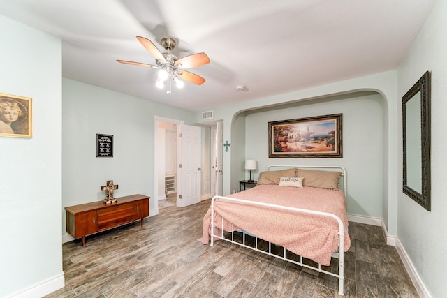 bedroom featuring visible vents, baseboards, wood finished floors, arched walkways, and a ceiling fan