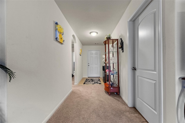 hallway with light colored carpet, baseboards, and arched walkways