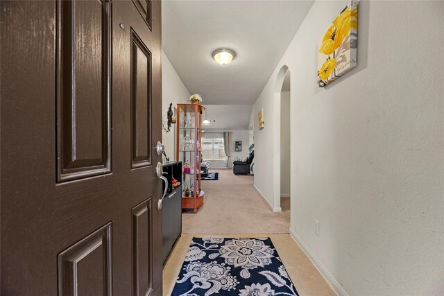 corridor with light tile patterned floors, baseboards, arched walkways, and light carpet