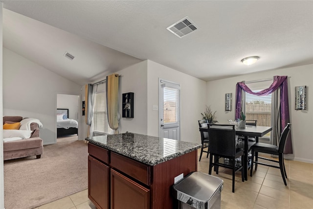 kitchen featuring vaulted ceiling, a kitchen island, visible vents, and light carpet