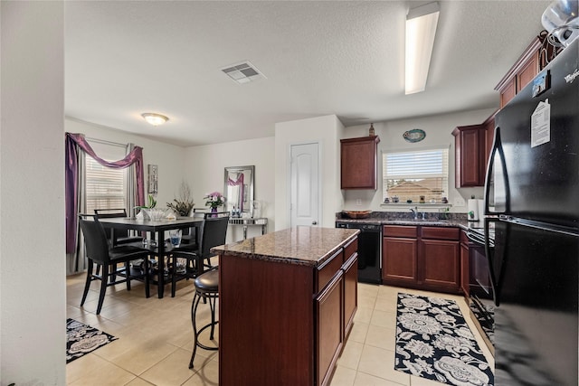kitchen with visible vents, black appliances, a kitchen island, dark stone counters, and light tile patterned floors