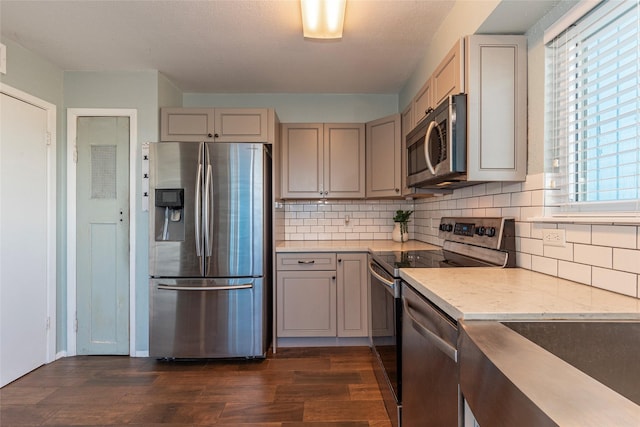 908 Calico Jack Cv, Galveston, TX 77554 - kitchen with appliances with stainless steel finishes, dark wood-type flooring, gray cabinetry, decorative backsplash, and light stone counters