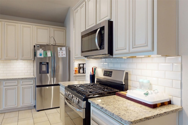 kitchen featuring stainless steel appliances, light stone counters, light tile patterned floors, and tasteful backsplash