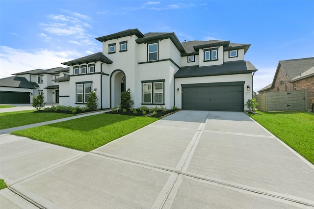 prairie-style house with a front lawn, fence, stucco siding, a garage, and driveway