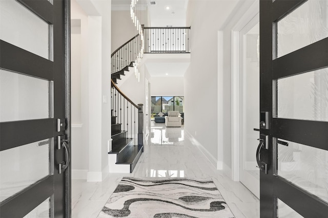 entrance foyer featuring marble finish floor, a high ceiling, stairs, and baseboards