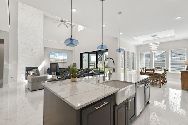 kitchen with marble finish floor, a sink, a tray ceiling, a stone fireplace, and dishwasher