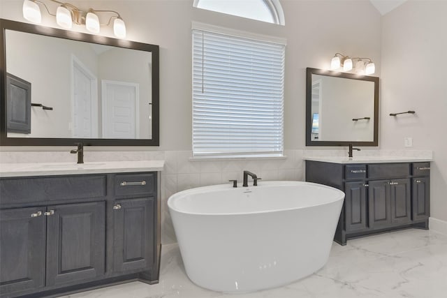 full bath with a freestanding tub, two vanities, marble finish floor, and a sink