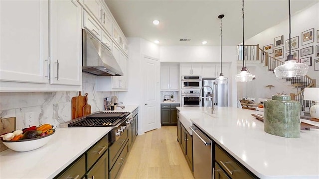 12043 Lake View Blvd, Mont Belvieu, TX 77523 - kitchen with under cabinet range hood, a large island with sink, stainless steel appliances, light countertops, and white cabinets