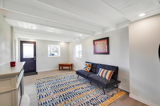 living room featuring beam ceiling, baseboards, and light wood-type flooring