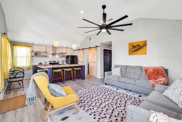 living room featuring a barn door, light wood-style floors, ceiling fan, and vaulted ceiling