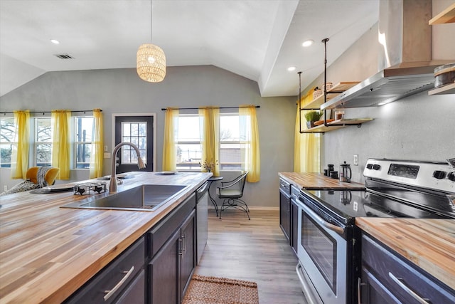 kitchen with butcher block countertops, stainless steel appliances, wall chimney range hood, and a sink