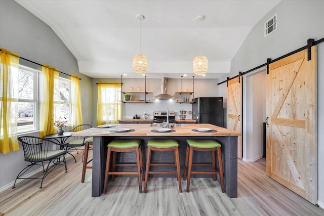 kitchen featuring visible vents, wall chimney range hood, butcher block countertops, a barn door, and freestanding refrigerator