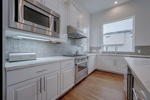 2414 Canal St Unit A, Houston, TX 77003 - kitchen with stainless steel appliances, under cabinet range hood, a sink, white cabinetry, and light wood-style floors