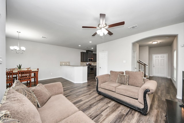 living area featuring visible vents, dark wood-type flooring, ceiling fan with notable chandelier, arched walkways, and baseboards