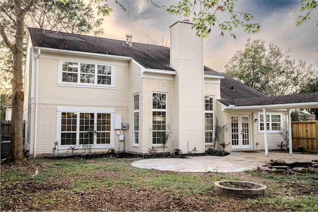 back of property at dusk with fence, french doors, brick siding, a chimney, and a patio area