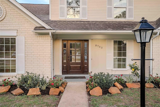 doorway to property featuring brick siding and roof with shingles