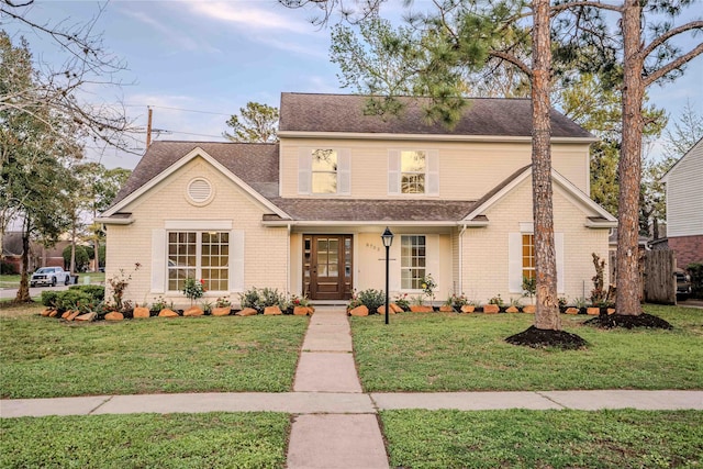 traditional-style home featuring brick siding, roof with shingles, and a front lawn