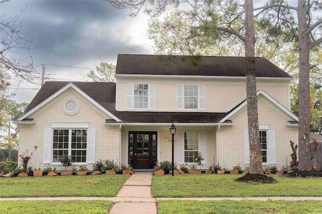 traditional-style house with brick siding, a shingled roof, and a front yard