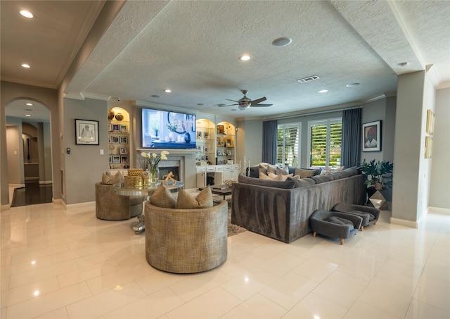tiled living room with a ceiling fan, visible vents, arched walkways, a lit fireplace, and crown molding
