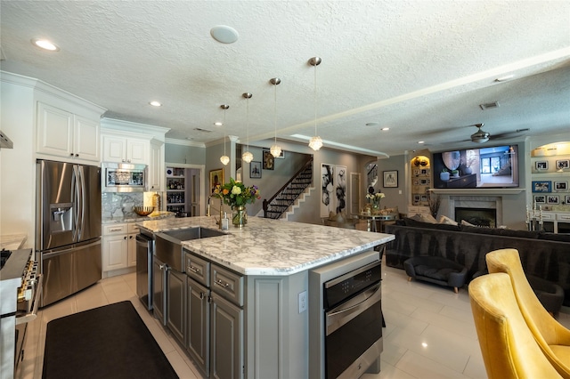 kitchen featuring appliances with stainless steel finishes, a fireplace, white cabinetry, a ceiling fan, and a sink