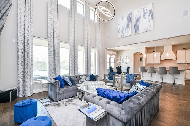 living room featuring arched walkways, plenty of natural light, a high ceiling, and dark wood finished floors