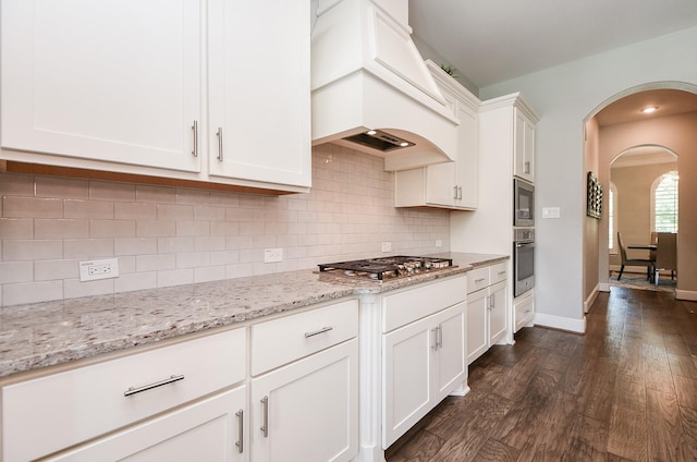 kitchen featuring custom range hood, dark wood-style floors, stainless steel appliances, arched walkways, and white cabinetry