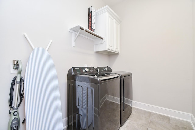 clothes washing area featuring cabinet space, light tile patterned floors, washing machine and dryer, and baseboards