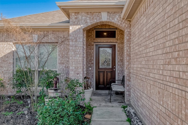 view of exterior entry featuring brick siding, stone siding, and a shingled roof