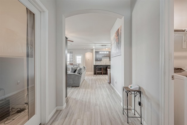 hallway featuring baseboards, arched walkways, washer / clothes dryer, and light wood finished floors