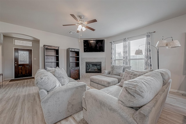 living room with a ceiling fan, visible vents, light wood finished floors, arched walkways, and a tiled fireplace