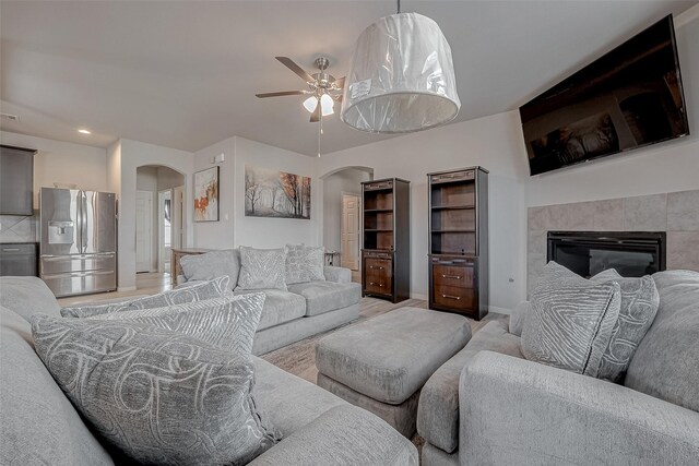living area with arched walkways, a fireplace, baseboards, and ceiling fan