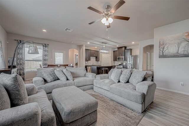living area with arched walkways, light wood finished floors, baseboards, and a ceiling fan