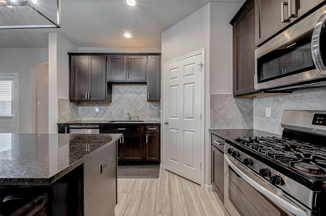 kitchen with dark brown cabinetry, dark stone counters, appliances with stainless steel finishes, arched walkways, and a sink
