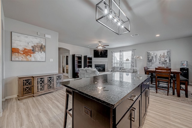 kitchen featuring arched walkways, visible vents, light wood-type flooring, and a glass covered fireplace