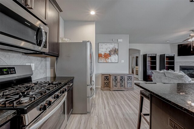 kitchen with a ceiling fan, dark stone countertops, stainless steel appliances, wine cooler, and dark brown cabinetry