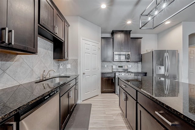kitchen featuring a sink, stainless steel appliances, dark brown cabinetry, and dark stone counters