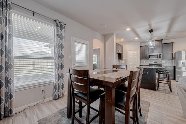 dining space featuring arched walkways, recessed lighting, light wood-type flooring, and baseboards