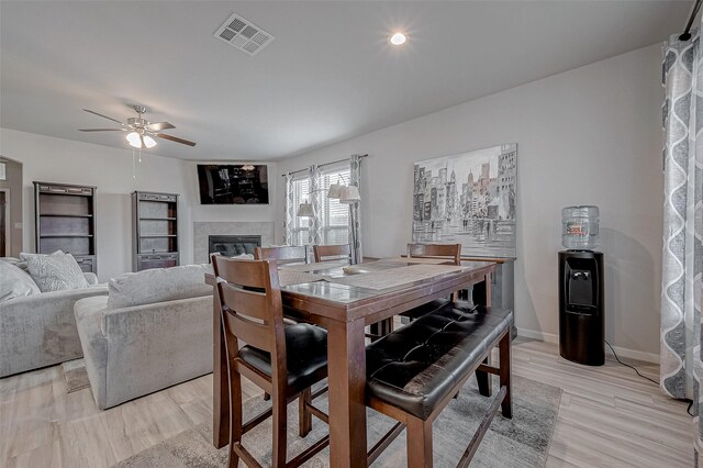 dining space featuring visible vents, baseboards, light wood-style flooring, a tile fireplace, and a ceiling fan