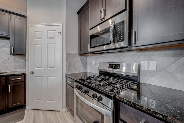 kitchen with dark stone countertops, light wood-style flooring, decorative backsplash, dark brown cabinets, and appliances with stainless steel finishes