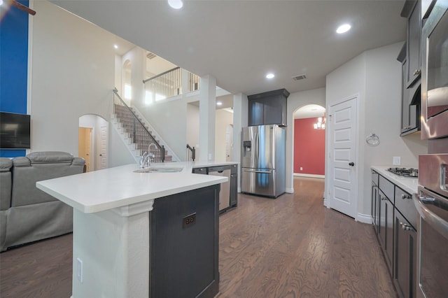 kitchen with dark wood-type flooring, light countertops, arched walkways, stainless steel appliances, and a sink