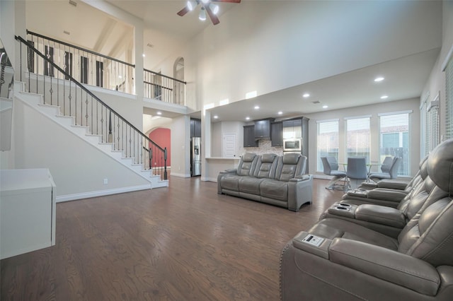 living room with a ceiling fan, dark wood finished floors, stairway, arched walkways, and baseboards