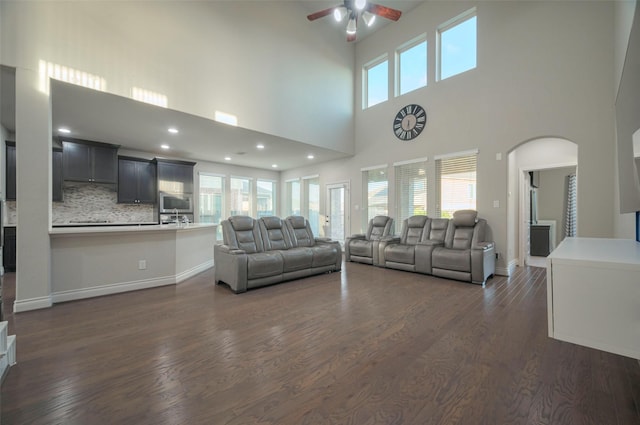 living room with dark wood finished floors, plenty of natural light, arched walkways, and ceiling fan