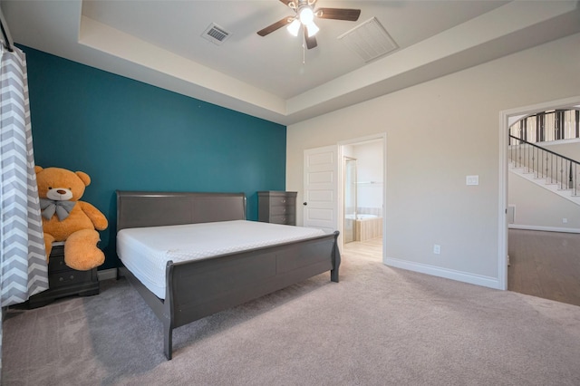 carpeted bedroom featuring visible vents, ceiling fan, baseboards, ensuite bathroom, and a raised ceiling