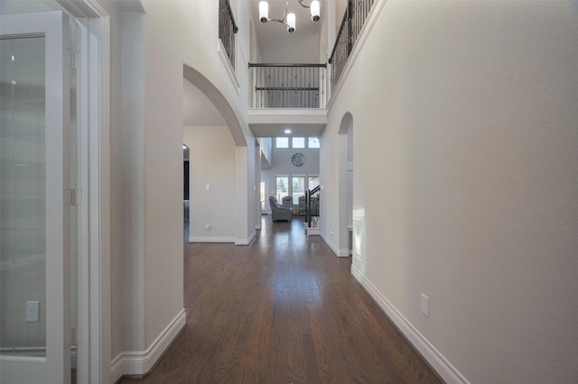 hallway with baseboards, arched walkways, dark wood-type flooring, a towering ceiling, and a chandelier