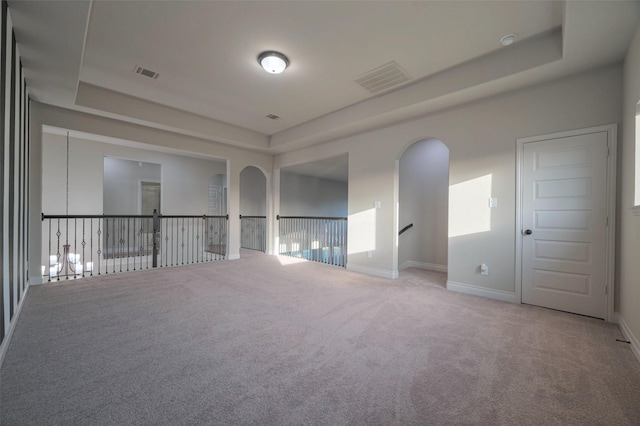 carpeted spare room featuring a raised ceiling, baseboards, and visible vents