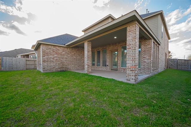 rear view of house with a yard, a patio, brick siding, and a fenced backyard